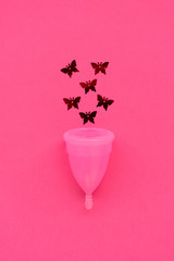 Pink menstrual cup with red glitters in butterfly shape on pink background. Female intimate hygiene concept. Top view