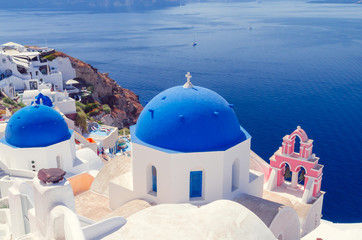 Oia Village, Santorini Cyclade islands, Greece. Beautiful view of a blue dome church and a pink towerbell.