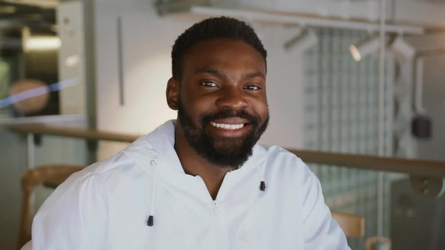 Portrait handsome young african american man look at camera smile cheerful enjoying successful startup business independent confidence contemporary workplace emotion interior relaxed slow motion