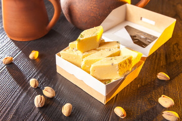 Halva and pistachios on the brown table. Halva with pistachios. A box of sweets with nuts. Sale of nuts and products containing nuts. Food industry. Production of sweets with nuts.