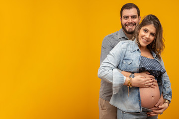 Couple in love, pregnant woman. Beautiful pregnant with her belly out. Couple on yellow background