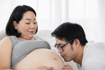 Fototapeta premium pregnant woman and her husband happy smiling while spending time together in the bedroom on white bed