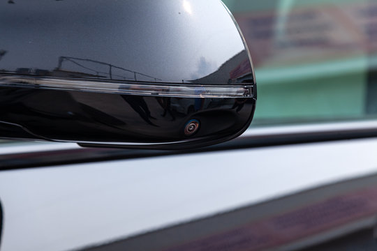 Close-up of the side left mirror with turn signal repeater, rear veiw 3d camera and window of the car body gray SUV on the parking after washing in auto service industry. Road safety while driving
