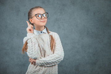 Close-up portrait of a beautiful excited schoolgirl with eyeglasses is isolated on the grey background