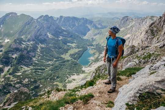 Handsome, strong man is climbing on Bobotov Kuk. Beautiful view with mountains, clouds and lake. Veliko Skrcko Lake in Durmitor National Park, Montenegro