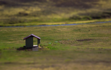 View of the small house on a green field with river on background. Tilt-Shift effect of the house with pass-through door. Landmannalaugar, Iceland
