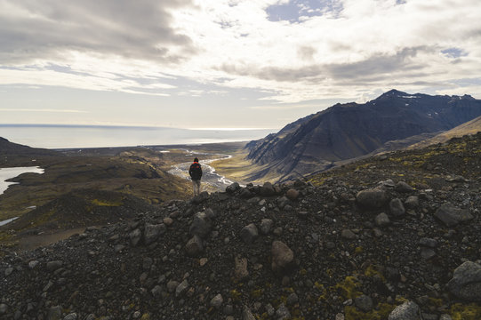 A hiker stands near the edge of a cliff at the base of J&ouml;klasel Glacier, overlooking the valley towards the Southern Region of Iceland.