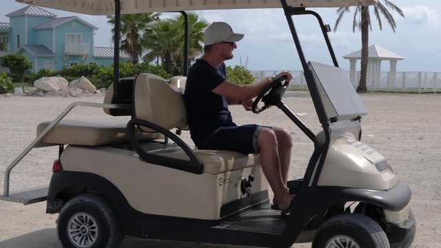 Caucasian man driving a golf cart on the coast land of Bahamas, medium shot