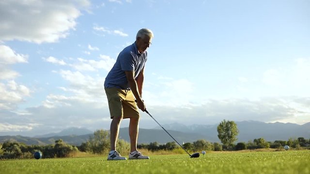 Cinematic Wide Angle Slow Motion shot of a man about to drive a ball off of a teebox. A bird can be seen flying behind the man.