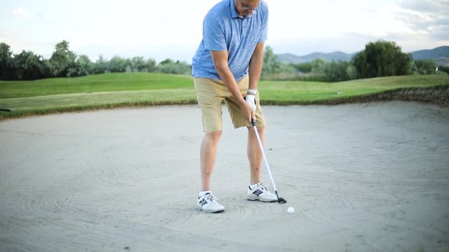 A male golfer preparing to hit his ball out of the sand trap onto the green. The golfer is playing on a nice resort golf course.