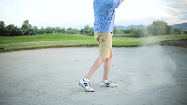 Cinematic Slow Motion shot of a golfer hitting the golf ball out of the sand trap and onto the green. The golfer is playing on a nice resort golf course.