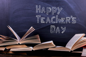 Open books are a stack on the desk, against the background of a chalk board. Difficult homework at school, a mountain of knowledge.