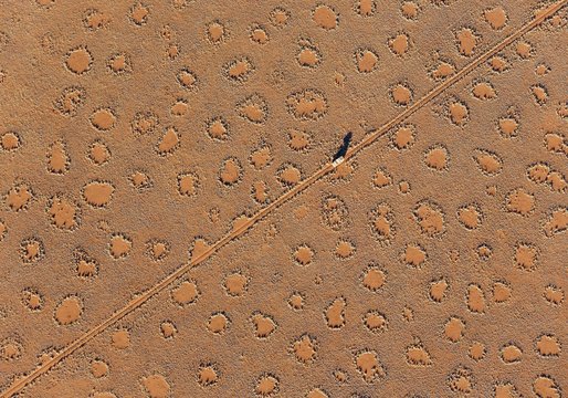 A vehicle of the balloon ground crew crosses a sandy plain with so-called Fairy Circles at the edge of the Namib Desert, photographed from a hot-air balloon, NamibRand Nature Reserve, Namibia, Africa