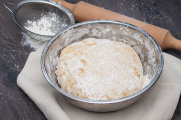 Raw dough with flour and accessories on the dark wooden table.