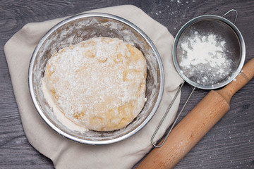 Raw dough with flour and accessories on the dark wooden table.