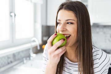 young brunette attractive woman cooking in kitchen in morning, eating green apple, smiling, happy mood, positive housewife, healthy lifestyle