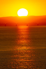 Early morning sunrise behind the mountains with sunlight reflection on the ocean/river. Landscape silhouette at dawn as the sun brings light to the sea coast. Start of the day with beautiful sunshine.