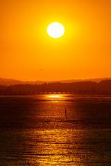 Early morning sunrise behind the mountains with sunlight reflection on the ocean/river. Landscape silhouette at dawn as the sun brings light to the sea coast. Start of the day with beautiful sunshine.