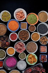 Bowls with species on black background. Hibiscus, yellow lentils, green lentils, pink arooz, star anise, chickpeas, sesame, oat seeds