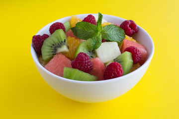 Fruit  salad in the white  bowl on the yellow  background. Closeup.