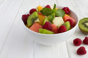 Fruit  salad in the white bowl on the white wooden background. Closeup.