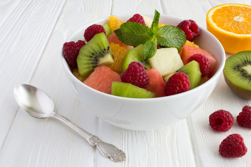 Fruit  salad in the white bowl on the white wooden background. Closeup.