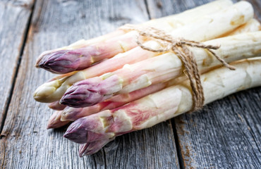 Roher weißer Spargel mit violetten Köpfen als Bündel auf einem alten rustikalen ausgebleichten...
