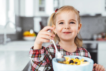 Smiling child girl drinking milk and eating corn flakes at the kitchen table