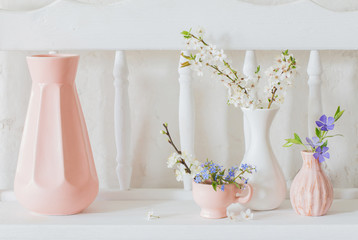 cups and vases with spring flowers on vintage wooden white shelf