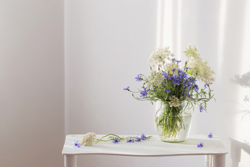 bouquet of cornflowers in jar on  white wooden shelf