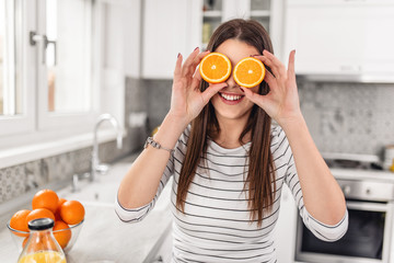 Portrait of a cheerful young girl holding two slices of an orange at her face over white wall background