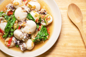Stir fried Cuttlefish or Cuttlefish Rainbow with basil on wooden table with spoon; top view. Thailand's popular dishes (Pad Ga Pow).