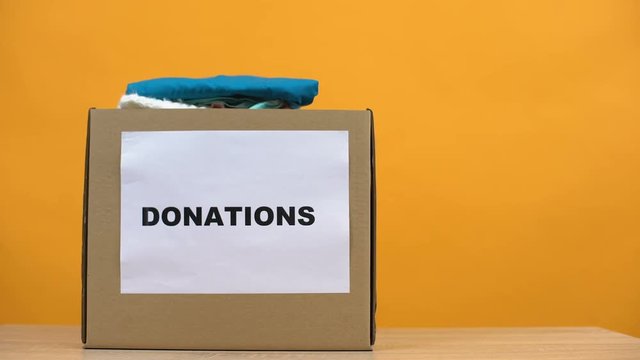 Female putting clothes in donation box on table, social activist kindness, help