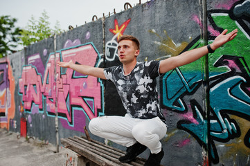 Lifestyle portrait of handsome man posing on the street of city with graffiti wall.