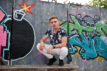 Lifestyle portrait of handsome man posing on the street of city with graffiti wall.
