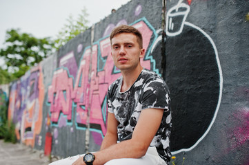 Lifestyle portrait of handsome man posing on the street of city with graffiti wall.