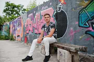 Lifestyle portrait of handsome man posing on the street of city with graffiti wall.