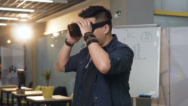 Japanese business man wearing virtual reality VR glasses for work in modern bright office.