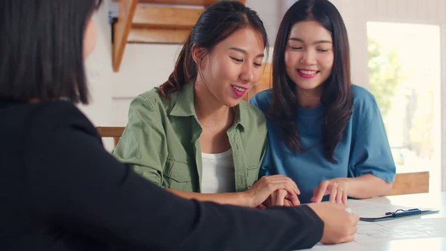 Asian Lesbian lgbtq women couple sign contract at home, Young couple consulting with real estate financial advisor, Buying new house and handshaking with broker in living room concept.