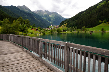 wooden bridge on beautiful lake of Lappago with flowers on foreground, Val Pusteria south tyrol (BZ) Italy