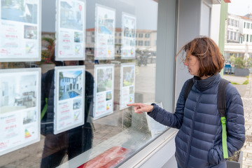 woman in front of shop real estate agency - obrazy, fototapety, plakaty