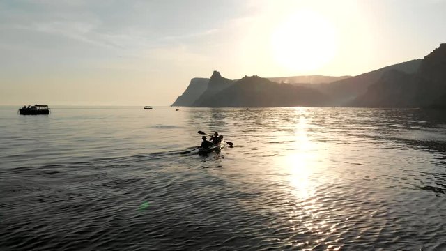 Kayakers paddling at sunset, aerial video. Drone flight above a kayak in the middle of the sea. Two people kayakers silhouette paddling at sunset. Colorful sport kayak silhouette.