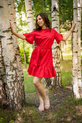 Beautiful brunette in a red dress walking in a Sunny Park