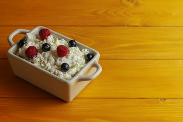 Bowl with cottage cheese and fresh berries on wooden table