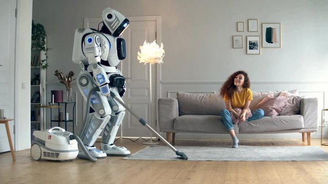 Young woman is watching a robot hoovering a room