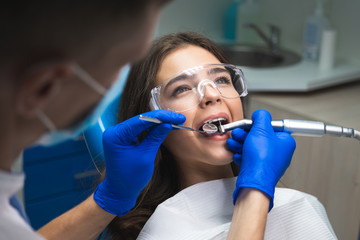 young brunette woman patient examined by dentist in blue gloves and medical mask using dental...