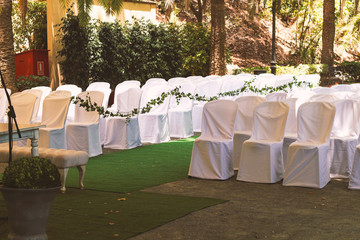 rows of chairs in white capes for guests at a wedding ceremony event outside in the park in the shade of trees, a romantic place under a canopy