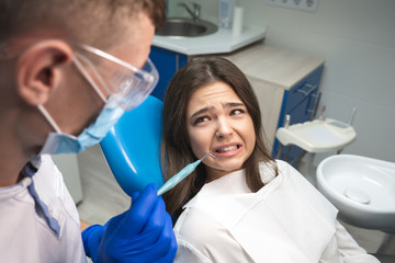 beautiful young frightened brunette woman patient having examination at dental office by handsome dentist in mask and blue gloves