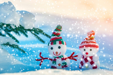 Two small funny toys baby snowman in knitted hats and scarves in deep snow outdoors on bright blue and white copy space background. Happy New Year and Merry Christmas greeting card.