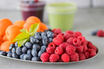 Fruit and berry smoothies and green smoothie. Fresh apricots, raspberries and blueberries on an oval metal plate. Gray background.